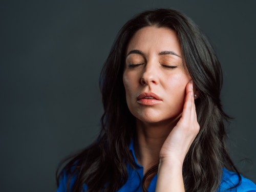 Gelangweilte reife Frau mit langen Haaren und Kopfschmerzen, Studioaufnahme. Mädchen mit den Händen am Kopf, isoliert vor grauem Hintergrund. Konzept von Problemen und Kopfschmerzen.