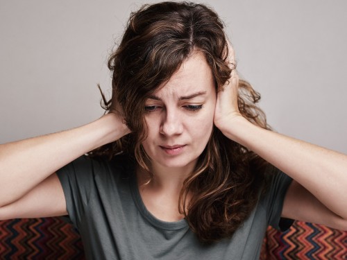 Frau bedeckt ihre Ohren mit den Händen, hat starke Kopfschmerzen, ist erschöpft und gestresst und leidet unter Depressionen.